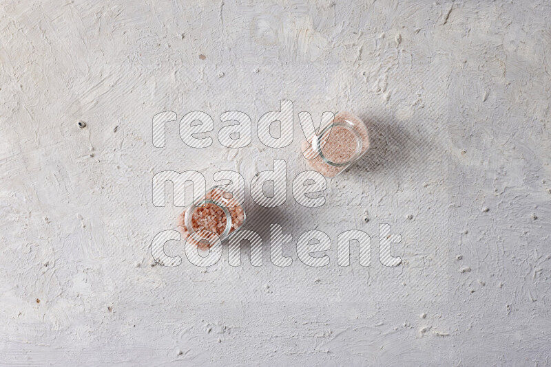 2 glass jars one is filled with fine himalayan salt and the other with coarse himalayan salt on white background