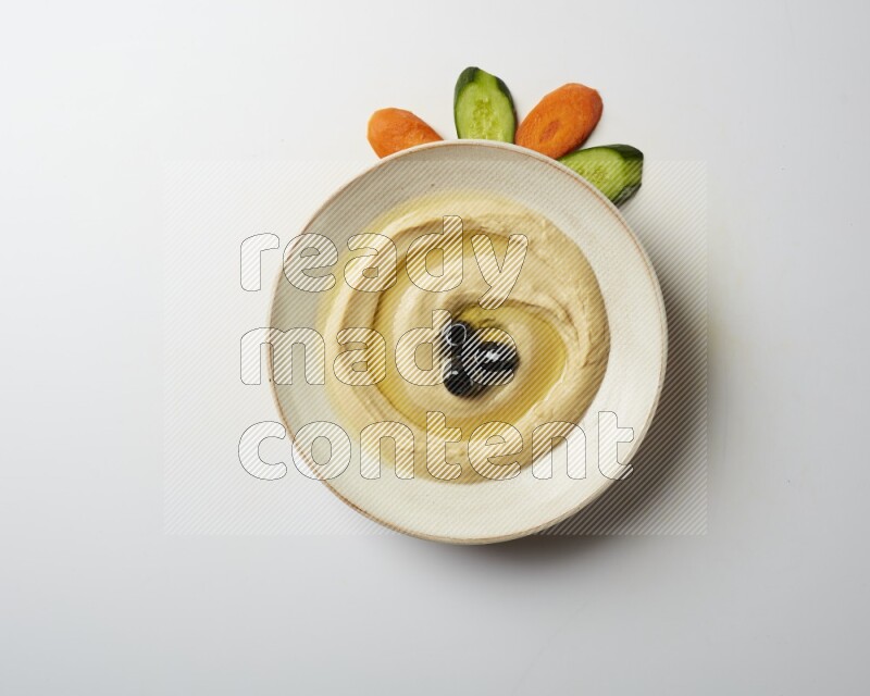 Hummus in a pottry plate garnished with black olives on a white background