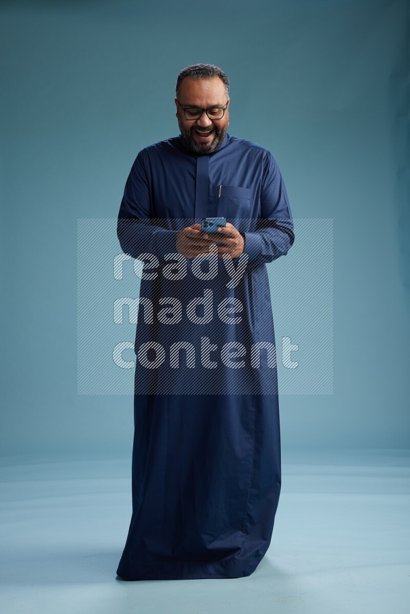 Saudi Man without shimag Standing texting on phone on blue background