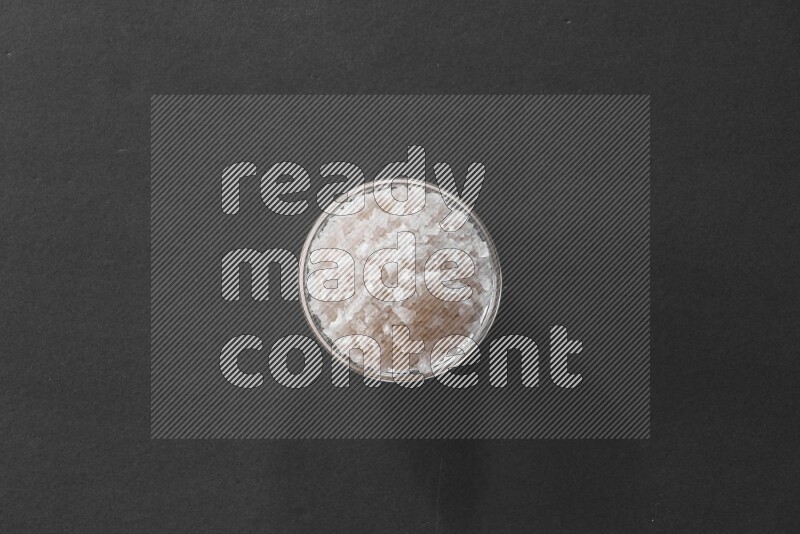 A glass bowl full of salt on black flooring
