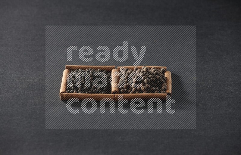2 squares of cinnamon sticks full of black peppers and allspice on black flooring