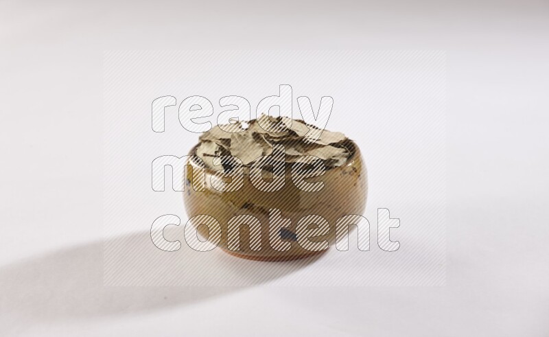 A multicolored pottery bowl full of dried bay leaves on white flooring in different angles