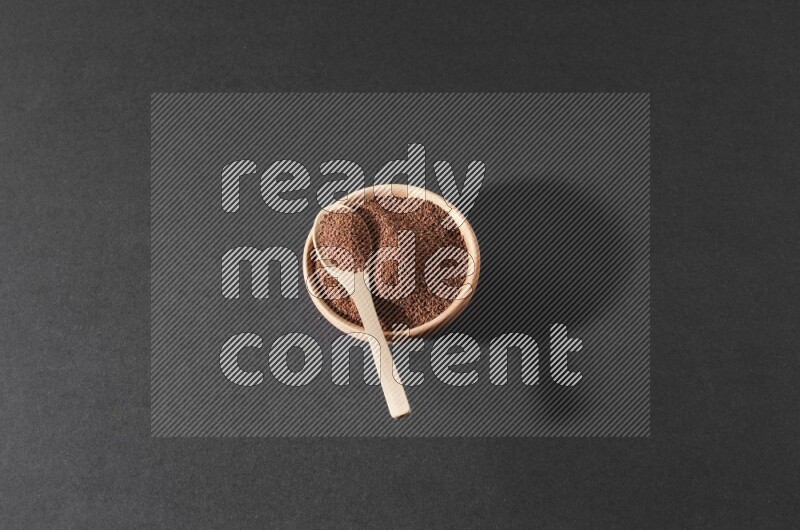 A wooden bowl full of garden cress seeds and a wooden spoon full of the seeds on it on a black flooring