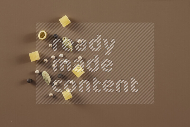 Raw pasta with different ingredients such as cherry tomatoes, garlic, onions, red chilis, black pepper, white pepper, bay laurel leaves, rosemary and cardamom on beige background