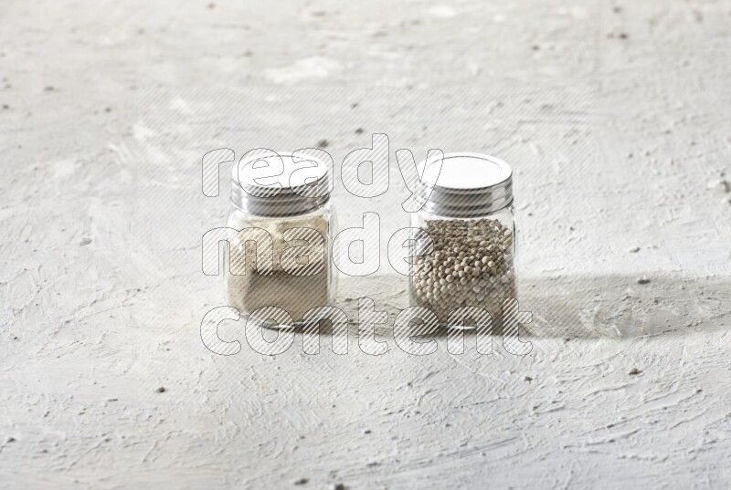 2 Herbal Glass jar full of white pepper beads and powder on textured white flooring