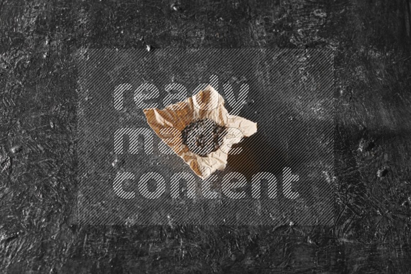 Black pepper beads on crumpled paper on a textured black flooring