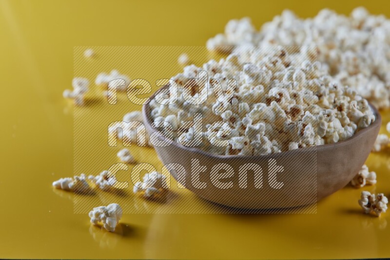 A brown pottery bowl full of popcorn with popcorn beside it on a yellow background in different angles