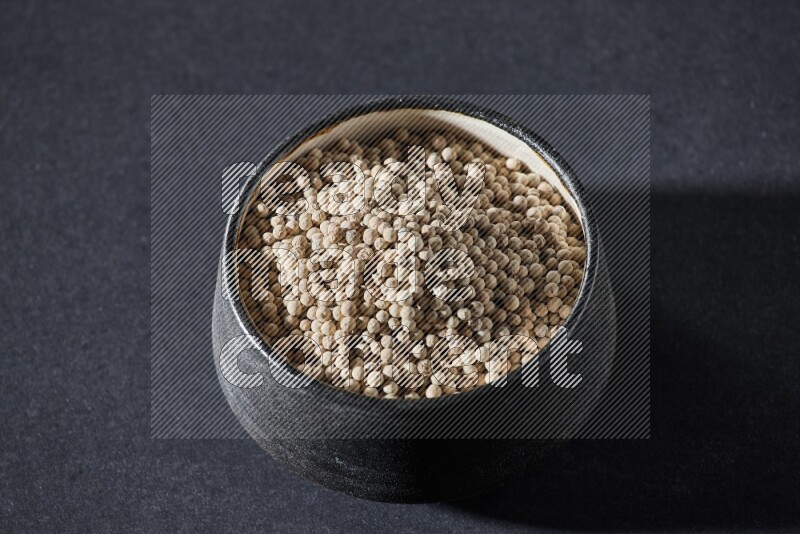 Black pottery bowl full of white pepper on black flooring