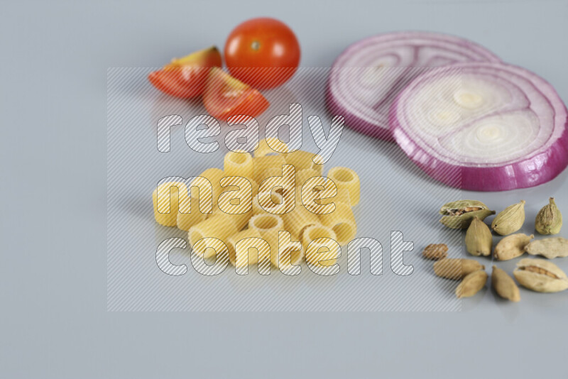Raw pasta with different ingredients such as cherry tomatoes, garlic, onions, red chilis, black pepper, white pepper, bay laurel leaves, rosemary, cardamom and mushrooms on light blue background