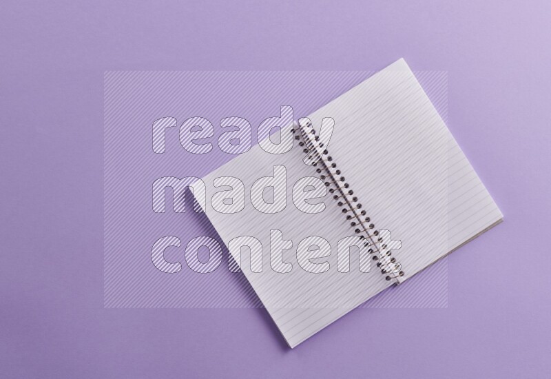 A blank open notebook with school supplies on purple background