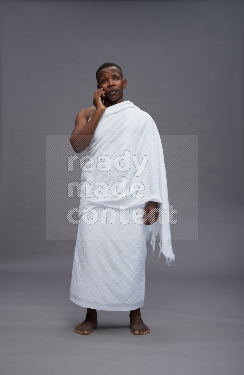 A man wearing Ehram Standing talking on phone on gray background