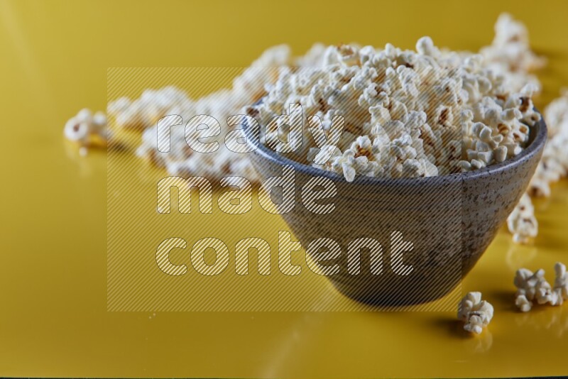 A multicolored pottery bowl full of popcorn with popcorn beside it on a yellow background in different angles