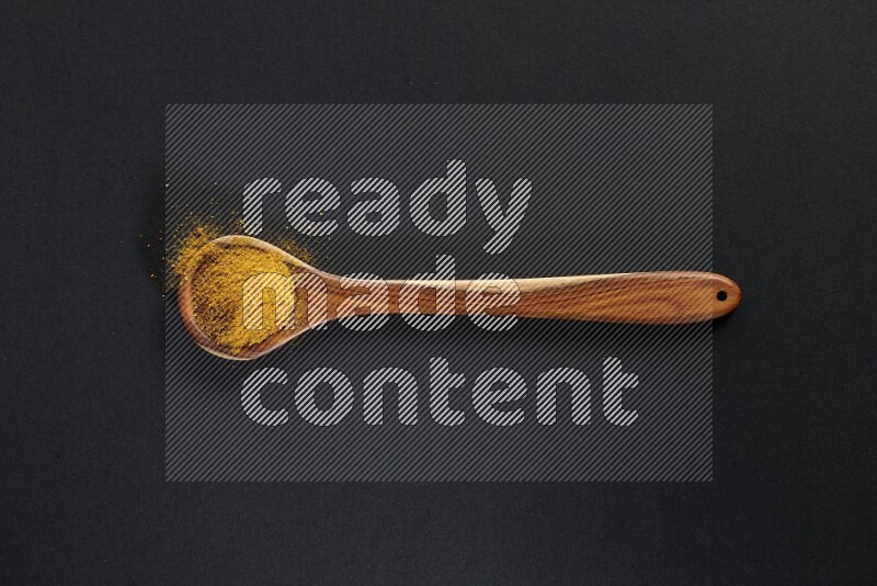 A wooden ladle full of turmeric powder on black flooring