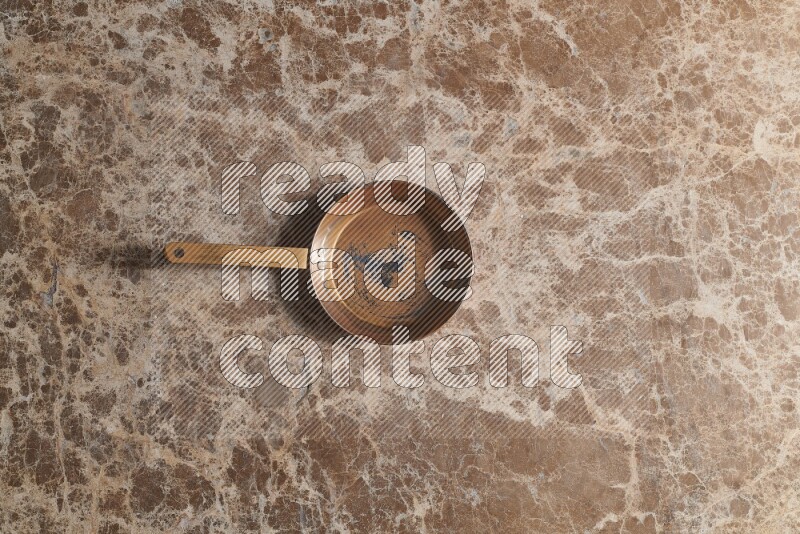 A small copper pan on beige marble background