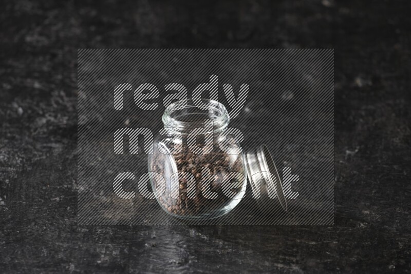 A glass spice jar full of cloves on textured black flooring