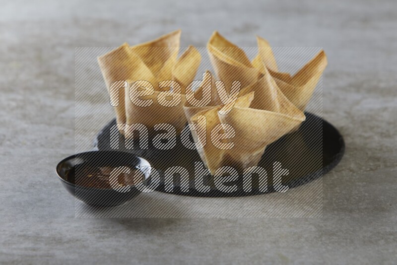 wonton cups with soy sauce ramkin on circle slate on grey textured counter top