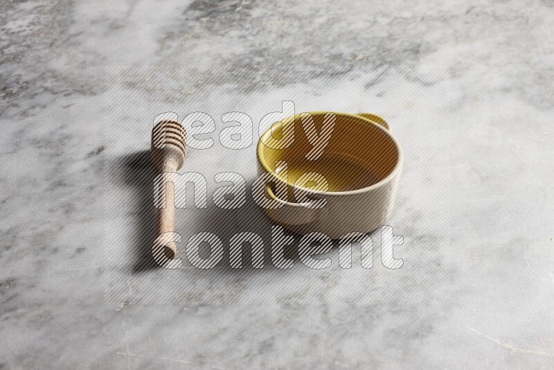 Multicolored pottery bowl with wooden honey dipper on the side on grey marble background
