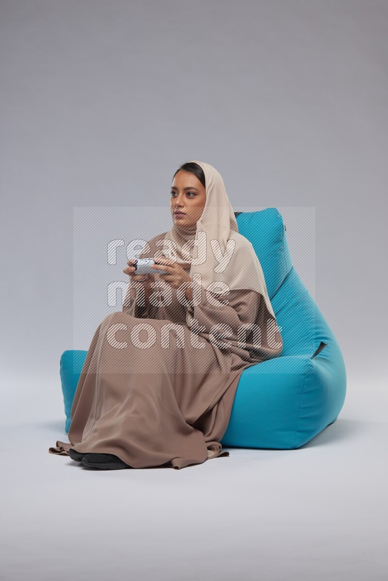 A Saudi woman sitting on a blue beanbag and gaming with joystick