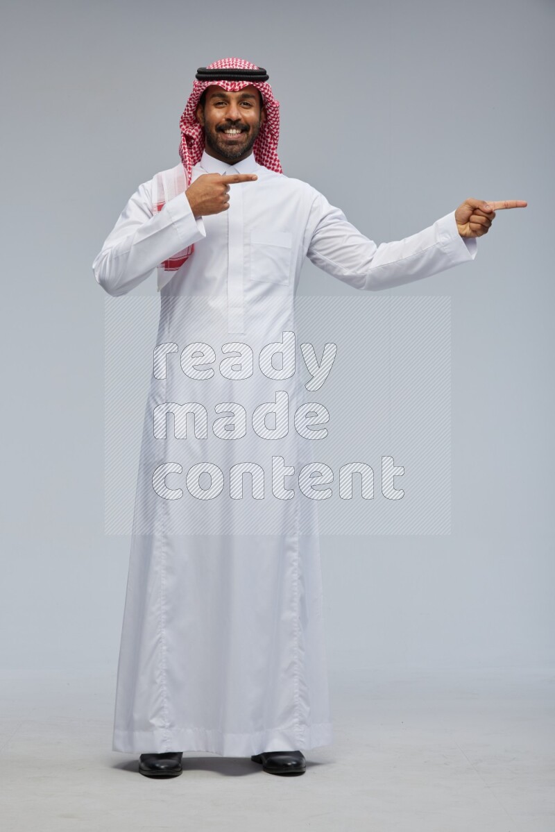 Saudi man Wearing Thob and shomag standing interacting with the camera on Gray background