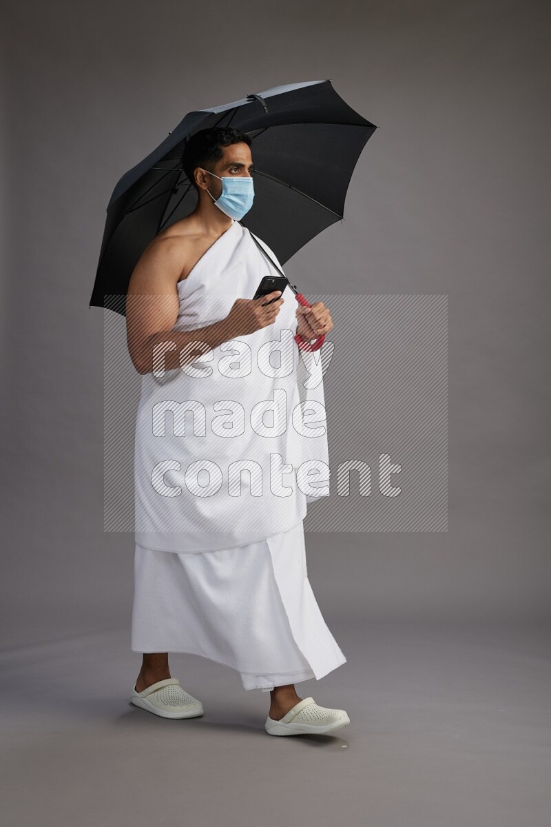 A man wearing Ehram and mask Standing holding umbrella on gray background on gray background