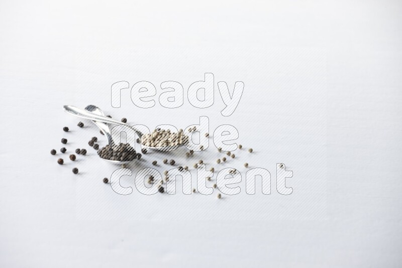 2 metal spoons full of black and white pepper beads with spreaded beads on white flooring