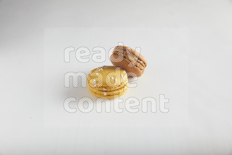 45º Shot of of two assorted Brown Irish Cream, and Yellow Piña Colada macarons on white background