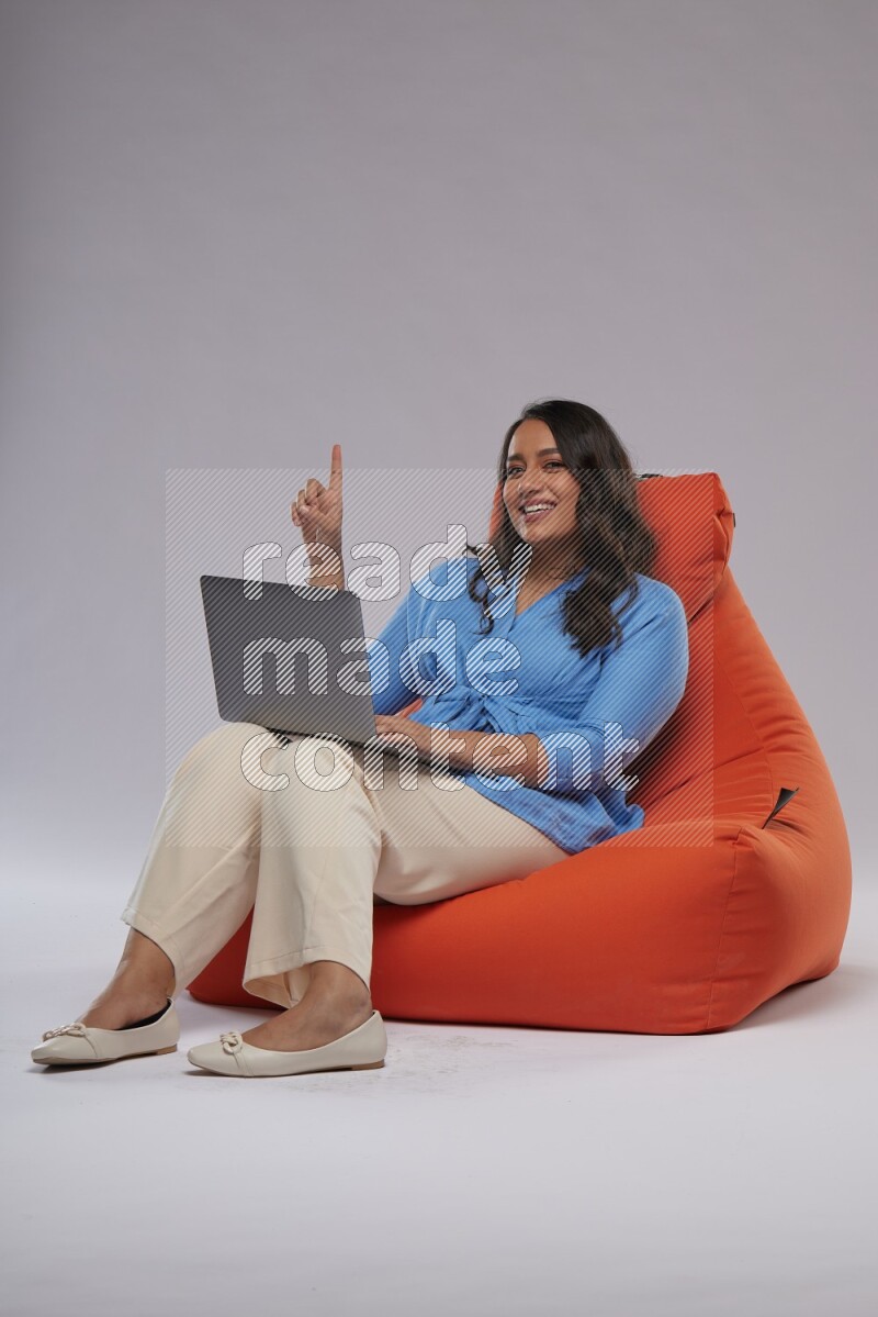A woman sitting on an orange beanbag and working on laptop