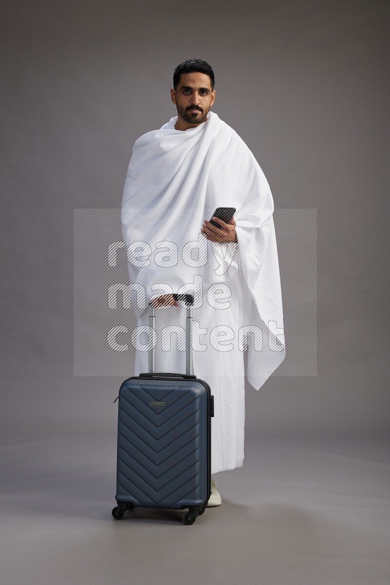 A man wearing Ehram Standing holding traveling bag on gray background
