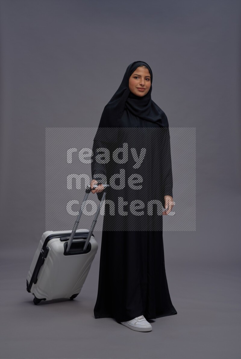 Saudi woman wearing Abaya standing holding bag on gray background
