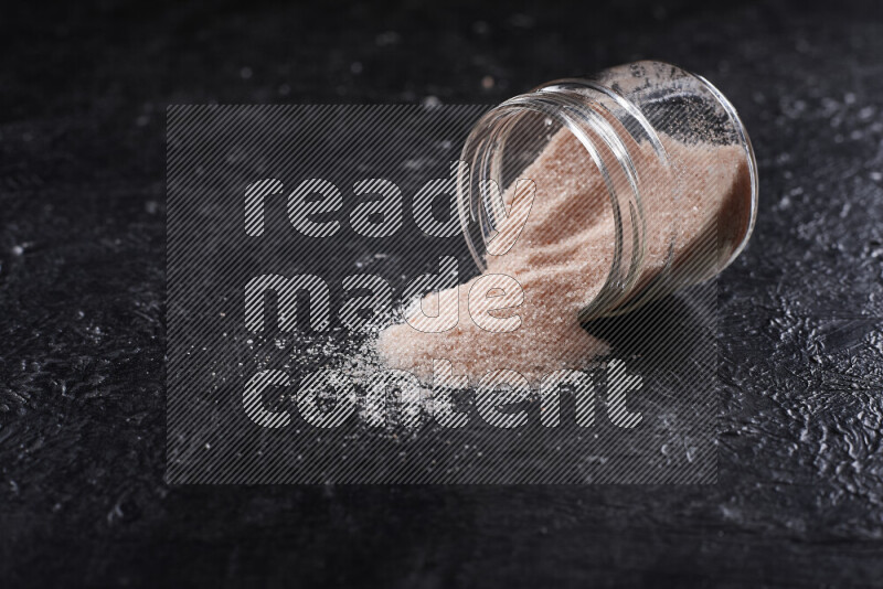 A glass jar full of fine himalayan salt on black background