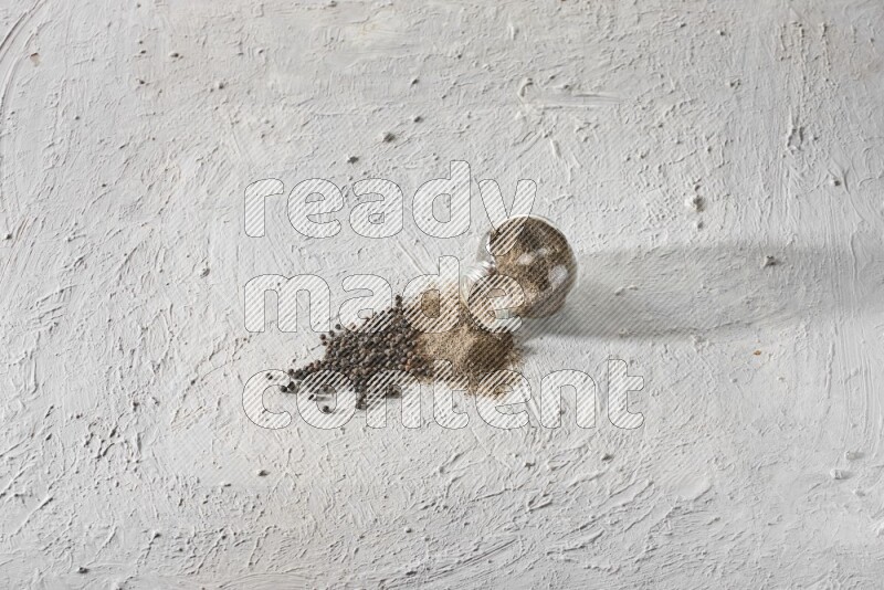 Flipped glass spice jar full of black pepper powder and paper beads beside it on a textured white flooring