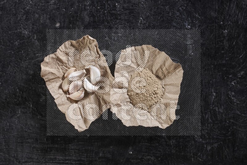 2 crumpled piece of paper full of garlic cloves and powder on a textured black flooring