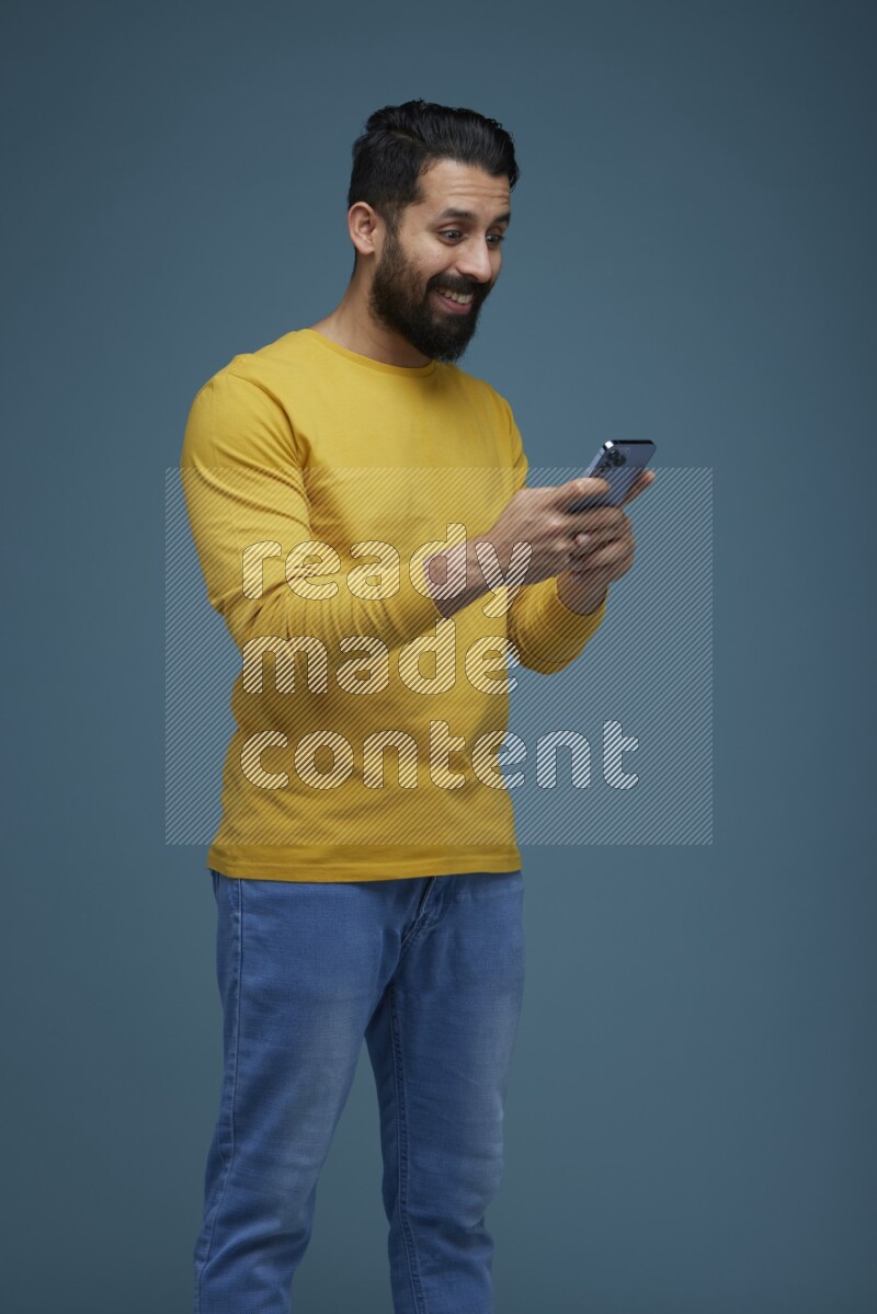 Man posing with a phone in a blue background wearing a yellow shirt