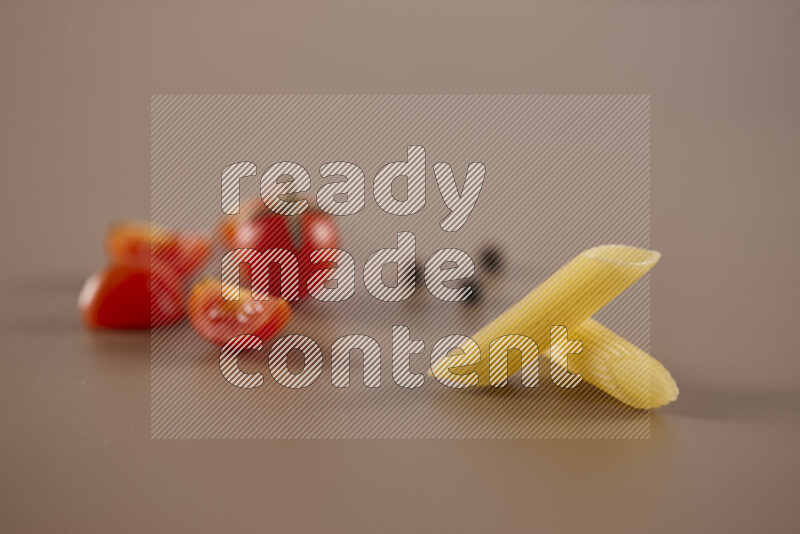 Raw pasta with different ingredients such as cherry tomatoes, garlic, onions, red chilis, black pepper, white pepper, bay laurel leaves, rosemary and cardamom on beige background