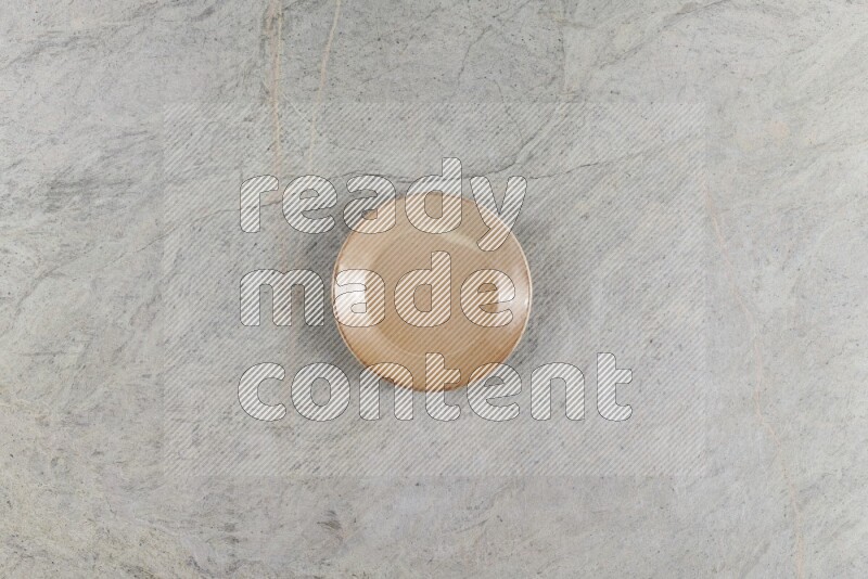 A circular beige pottery plate on grey marble background