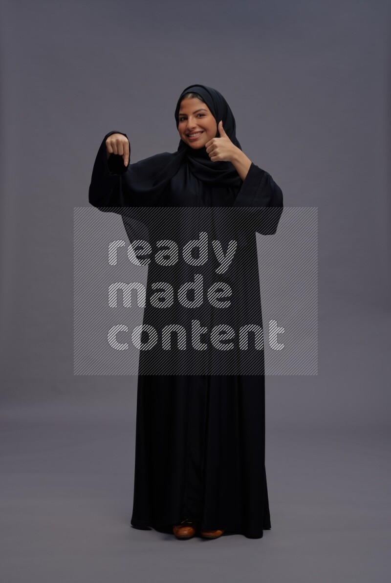 Saudi woman wearing Abaya standing interacting with the camera on gray background