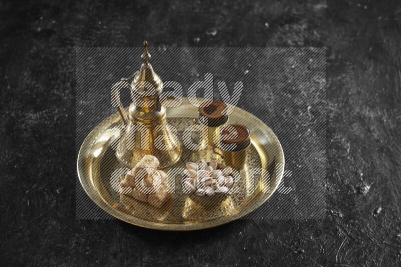 Oriental sweets with nuts and a drink on a metal tray in a dark setup