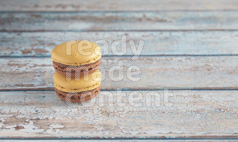45º Shot of two Yellow and Brown Chai Latte macarons on light blue wooden background
