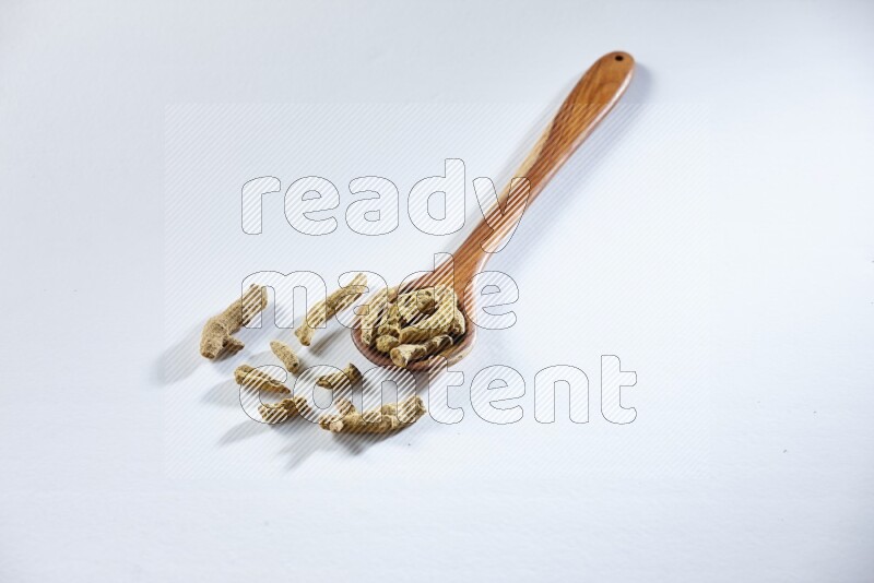 A wooden ladle full of dried turmeric fingers on white flooring