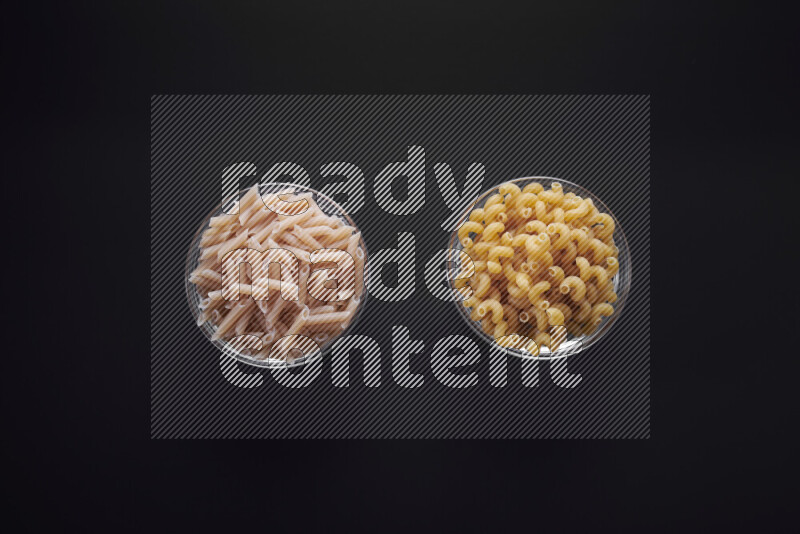 Different pasta types in glass bowls on black background