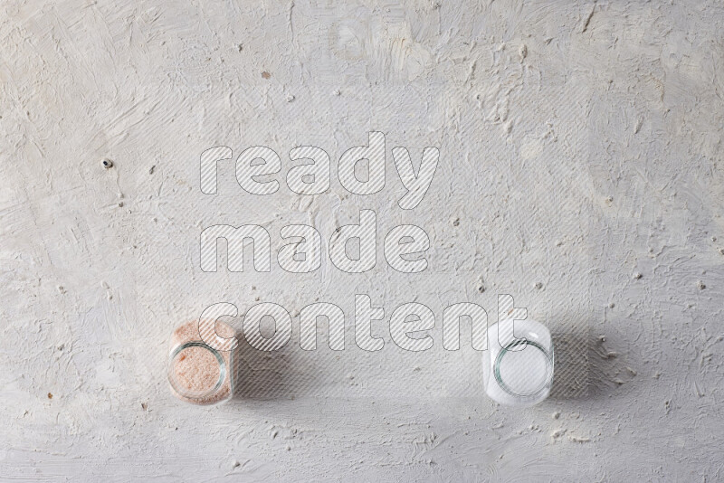 2 glass jars one is full of fine himalayan salt and the other with table salt on white background