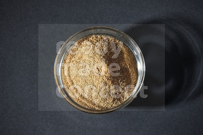 A glass bowl full of cumin powder on black flooring