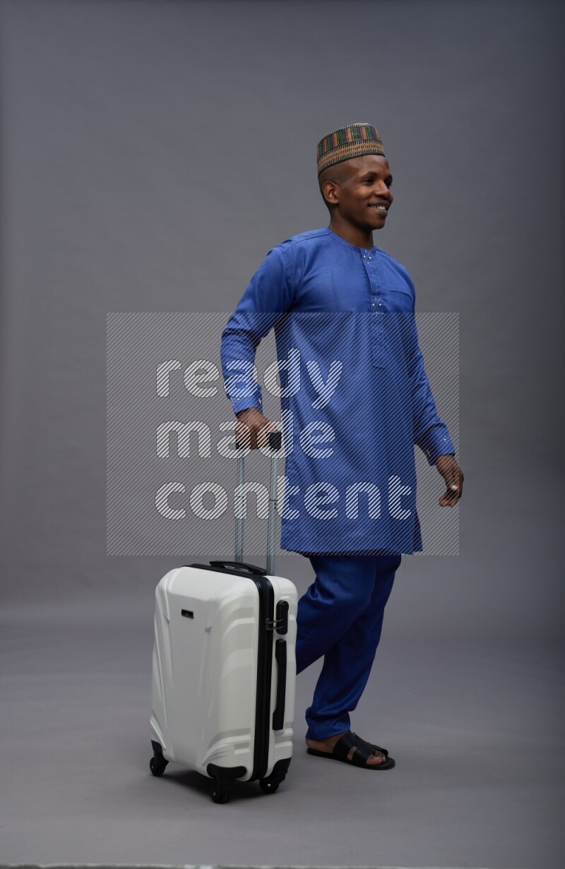 Man wearing Nigerian outfit standing holding bag on gray background