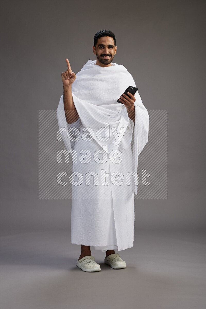 A man wearing Ehram Standing texting on phone on gray background