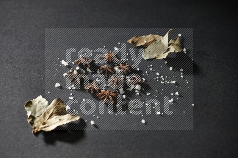 Salt, star anise and bay laurel on black flooring