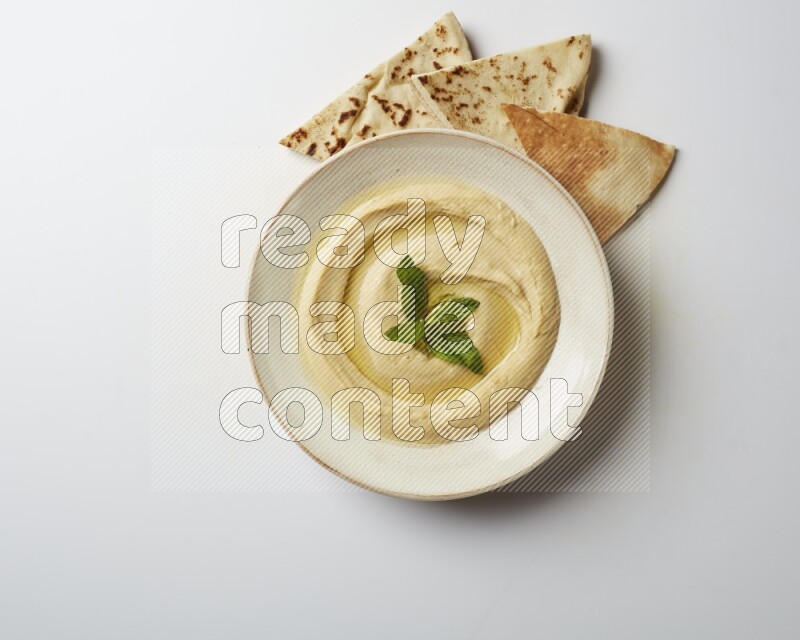 Hummus in a pottry plate garnished with mint  on a white background