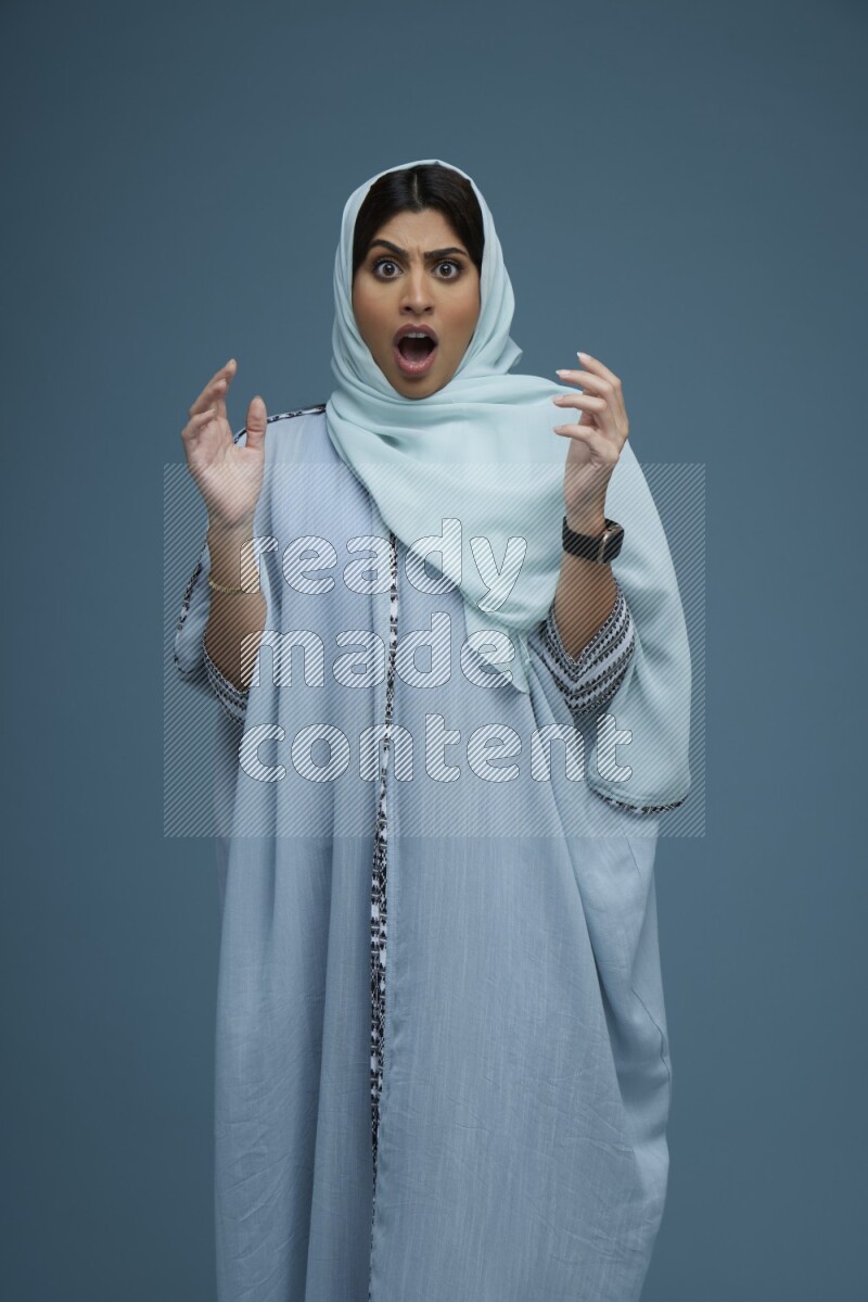 A woman posing in a blue background wearing a blue Abaya with hijab