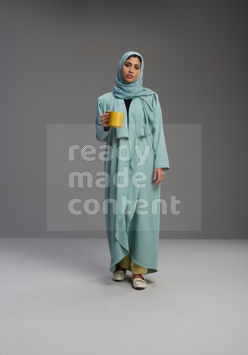 Saudi Woman wearing Abaya standing  holding a mug on Gray background