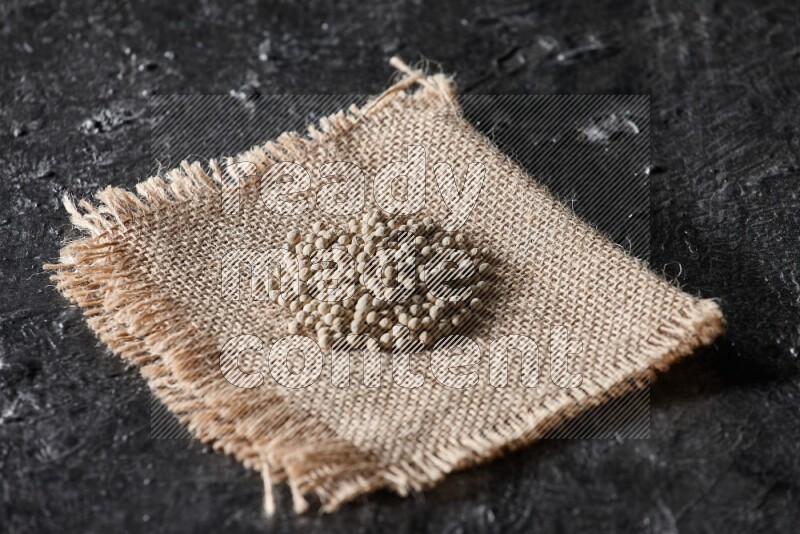 White pepper beads on a burlap piece of fabric on textured black flooring