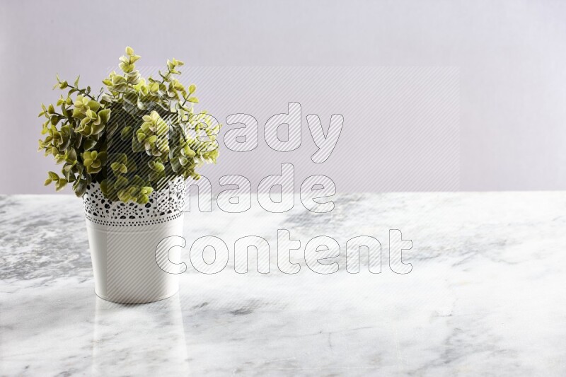 Green artificial plant in white decorative pot on grey marble background